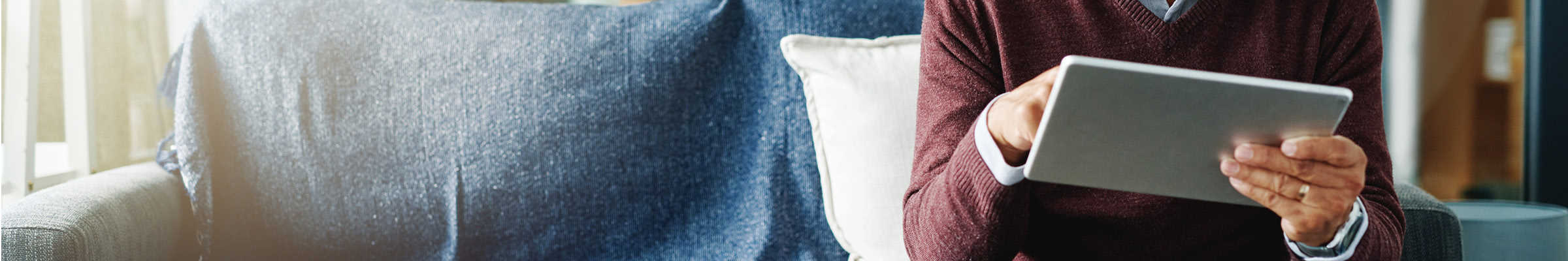 Cropped shot of male sitting on a couch holding an iPad.