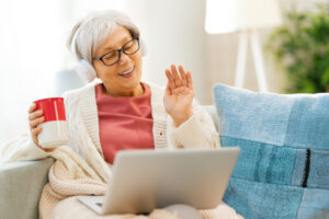 Joyful beautiful senior woman is using laptop sitting on the sofa at home.