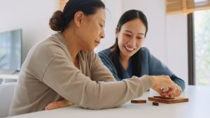 Asian caregiver nurse wearing blue scrubs and elderly woman retirement playing wooden shape puzzles game learning origami as for physiotherapy activity for dementia as a part of a physical therapy session Medical health care plan